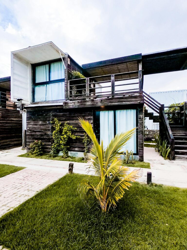 Contemporary two-story wooden house with lush greenery and palm plants.